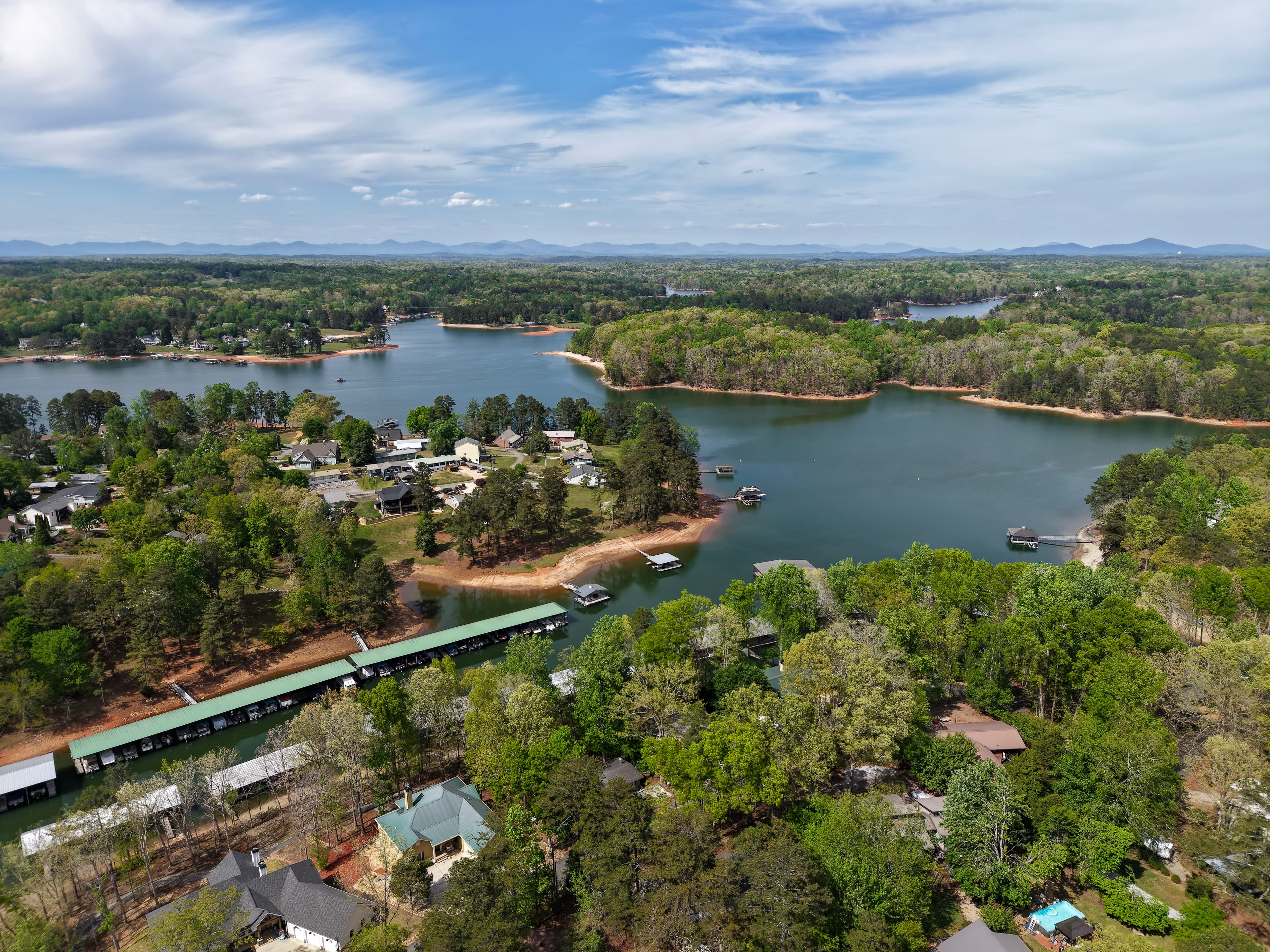 Aerial lake view with homes, docks, wooded shoreline, and distant mountains