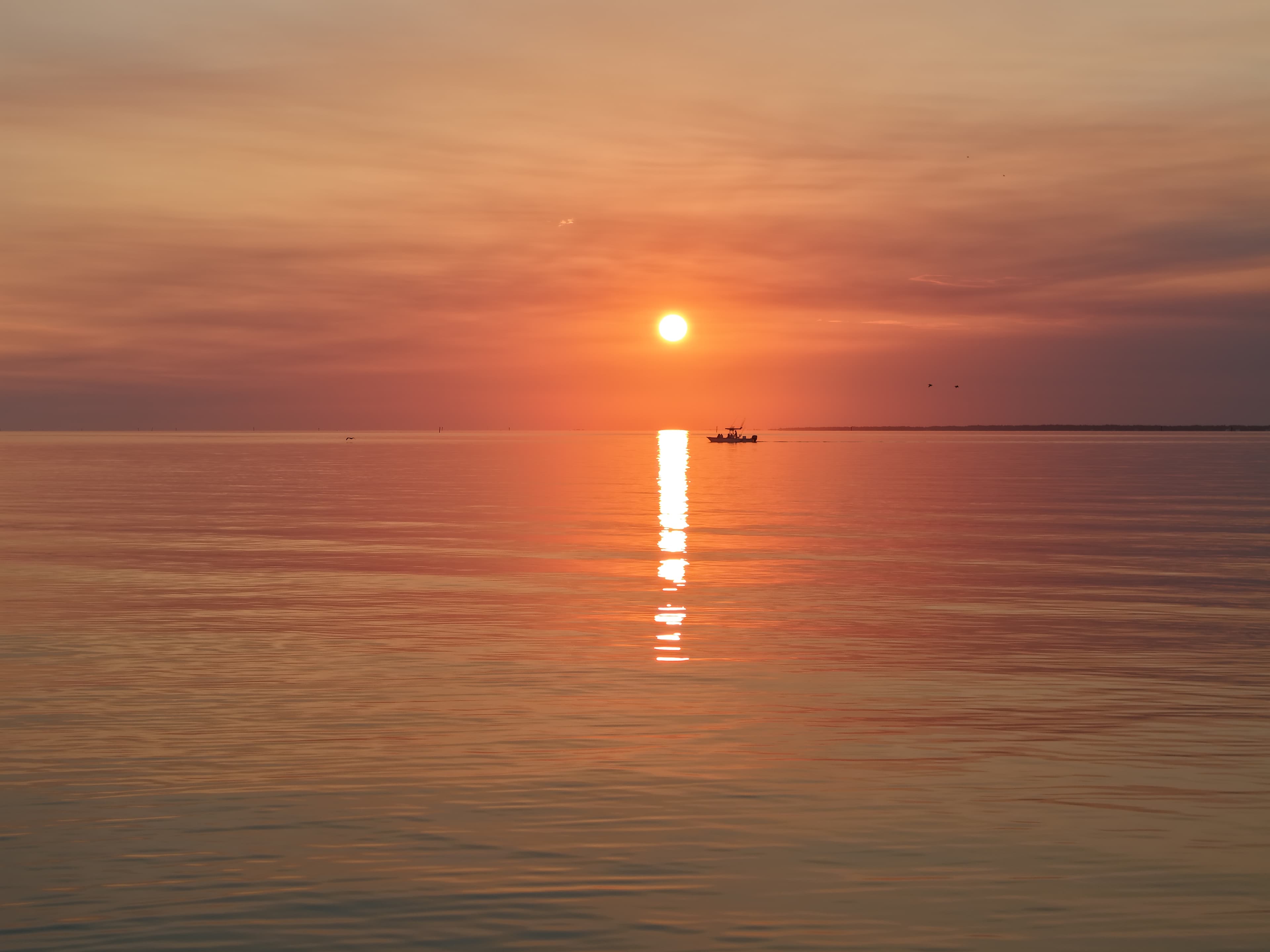 Sunset over calm ocean water with a bright reflection and a small boat in the distance